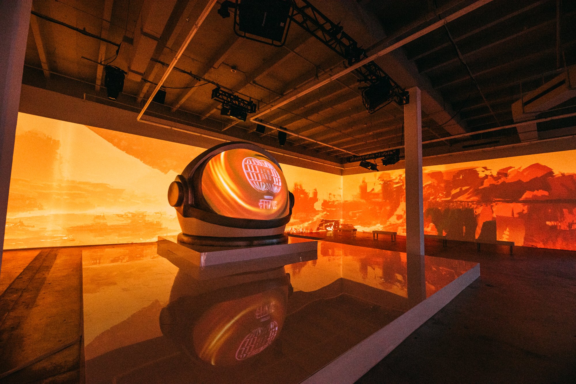 The Aku helmet sculpture in an orange projection-mapped room, reflected on the floor