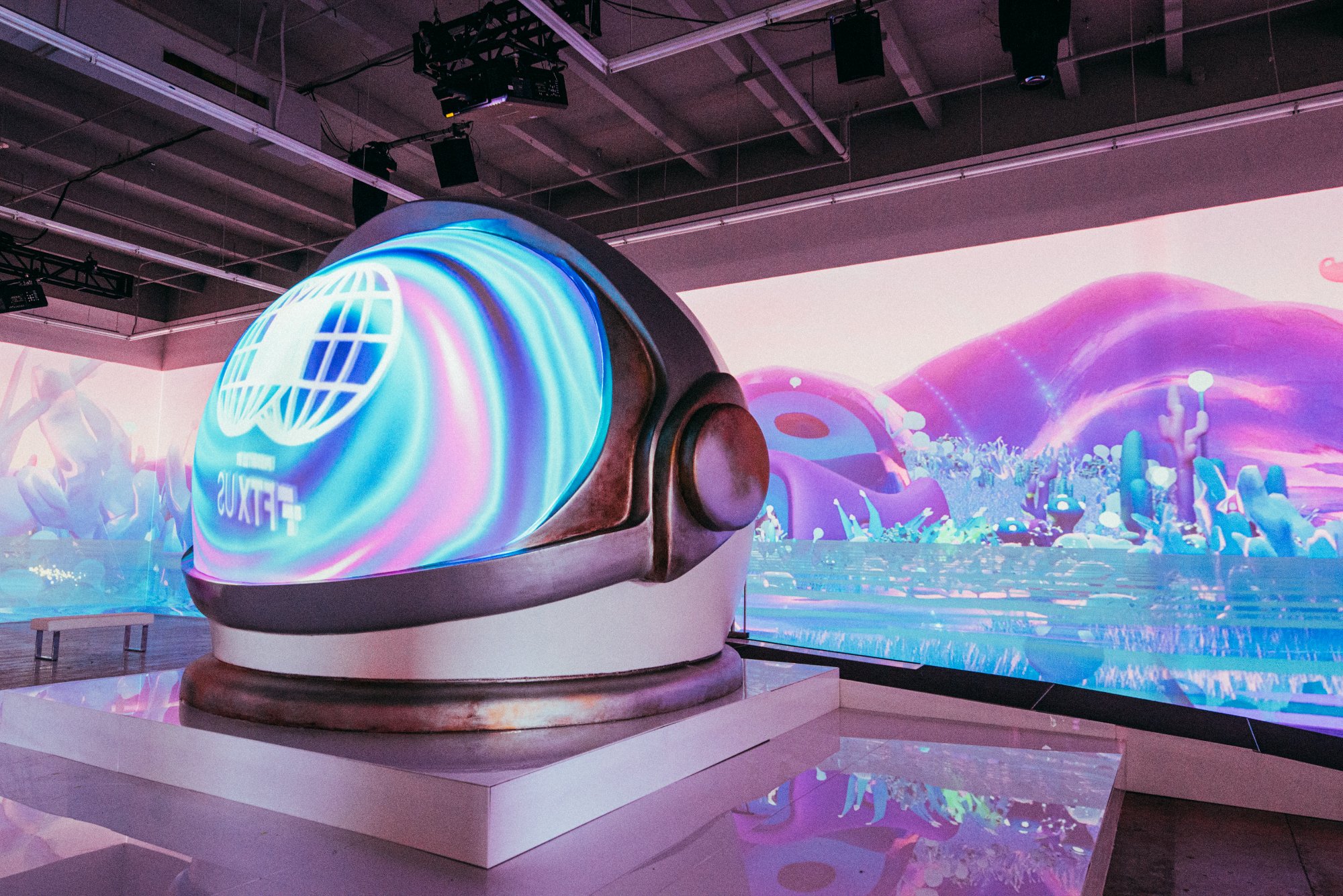 A colossal Aku helmet sculpture at the center, projection-mapped landscape walls around it