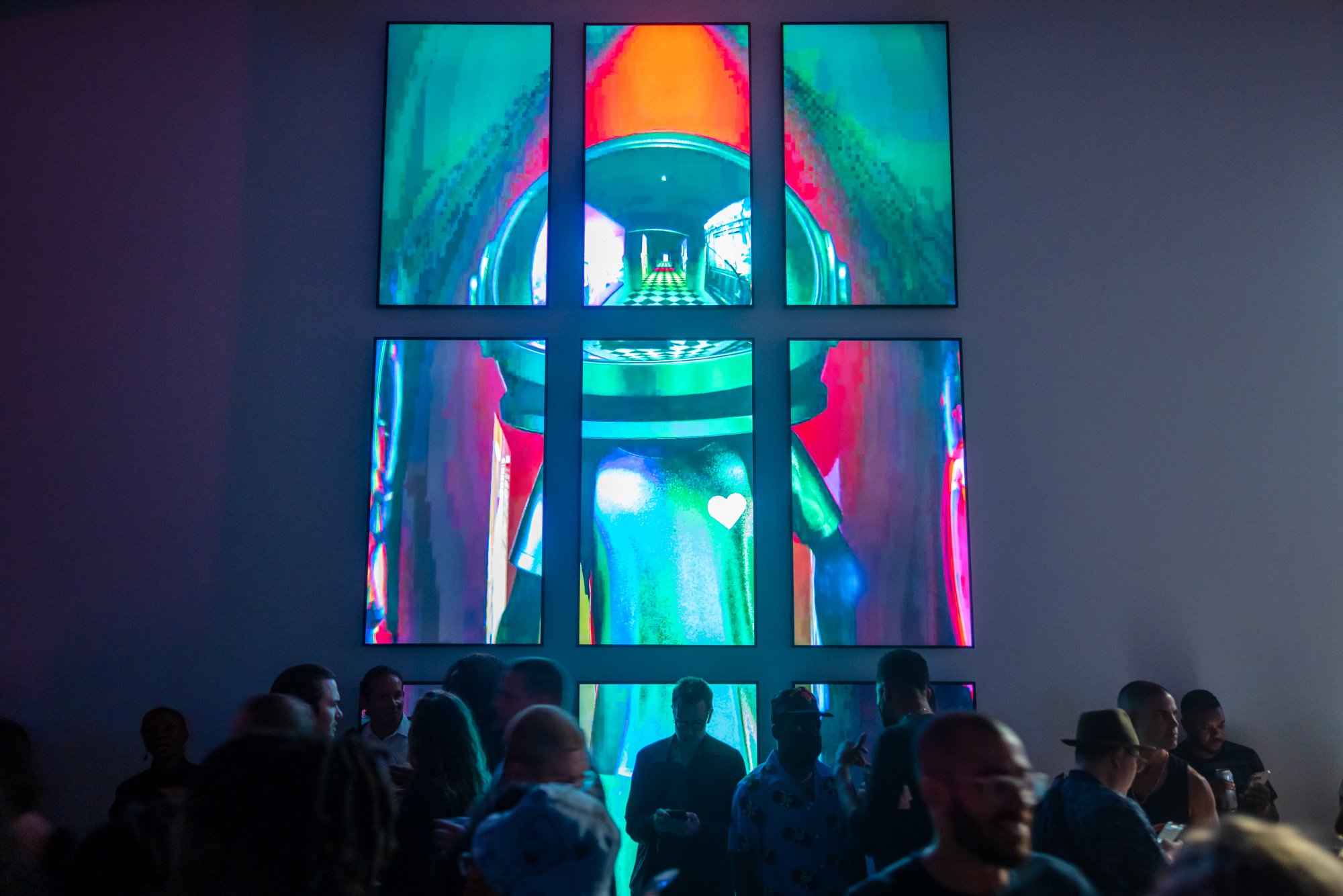Guests gathered before a towering grid of screens showing the Aku character