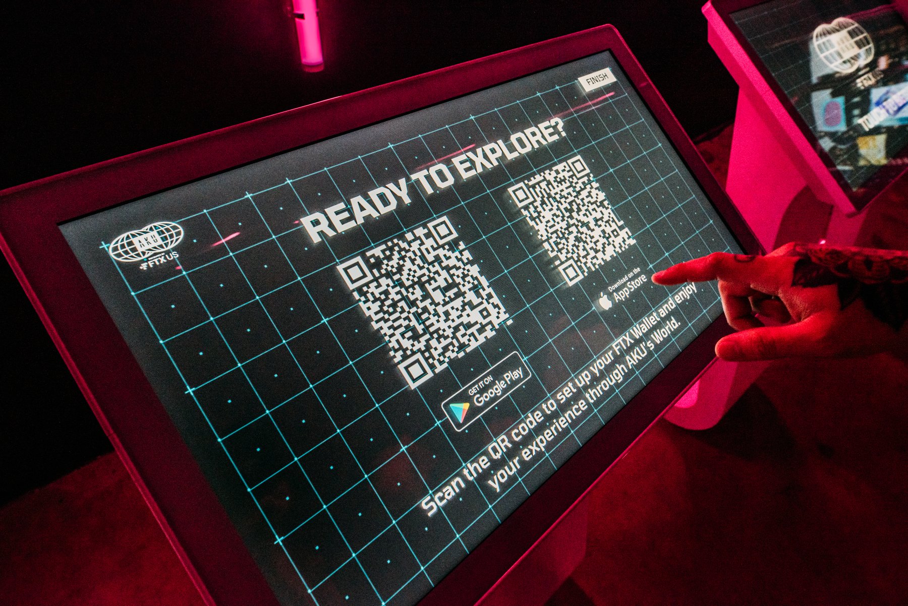 A kiosk screen reading Ready to Explore with QR codes, a hand reaching in