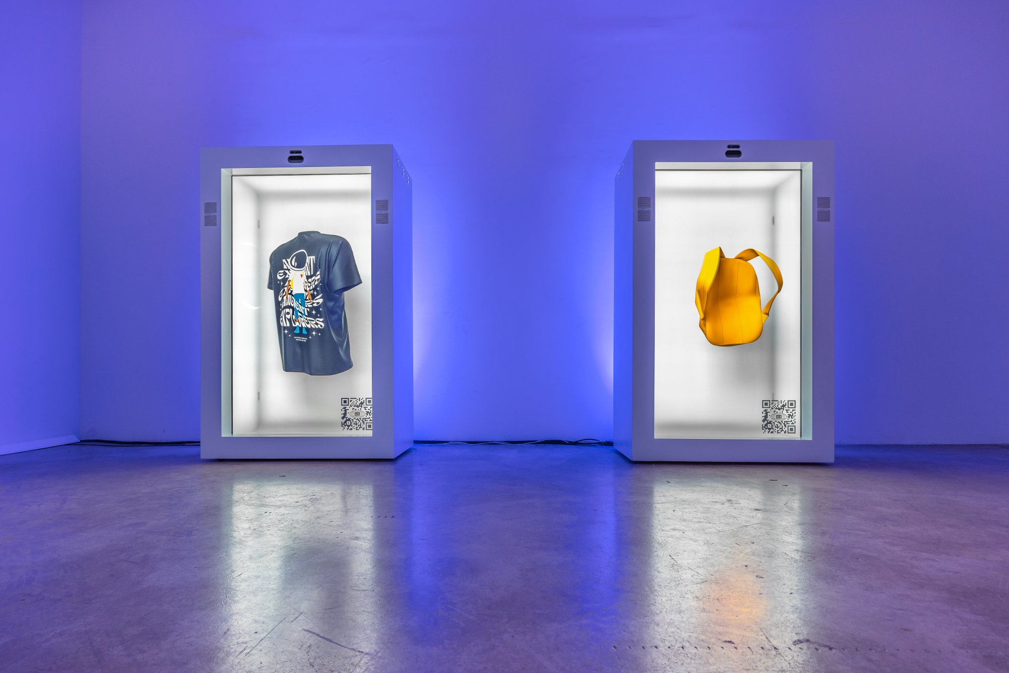 Two lit NFT display cases holding a t-shirt and a yellow backpack