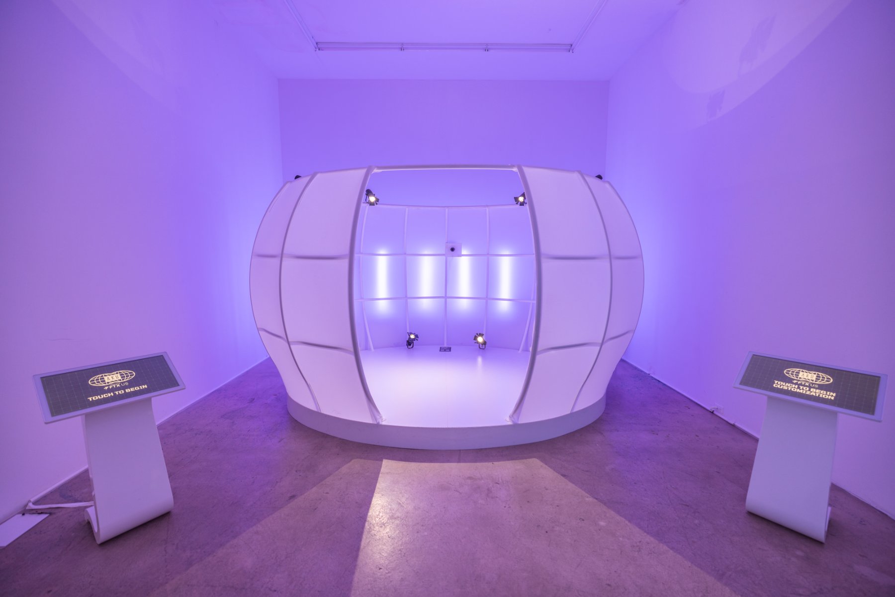 The white 4D-scanning pod with touch-to-begin kiosks in a purple room