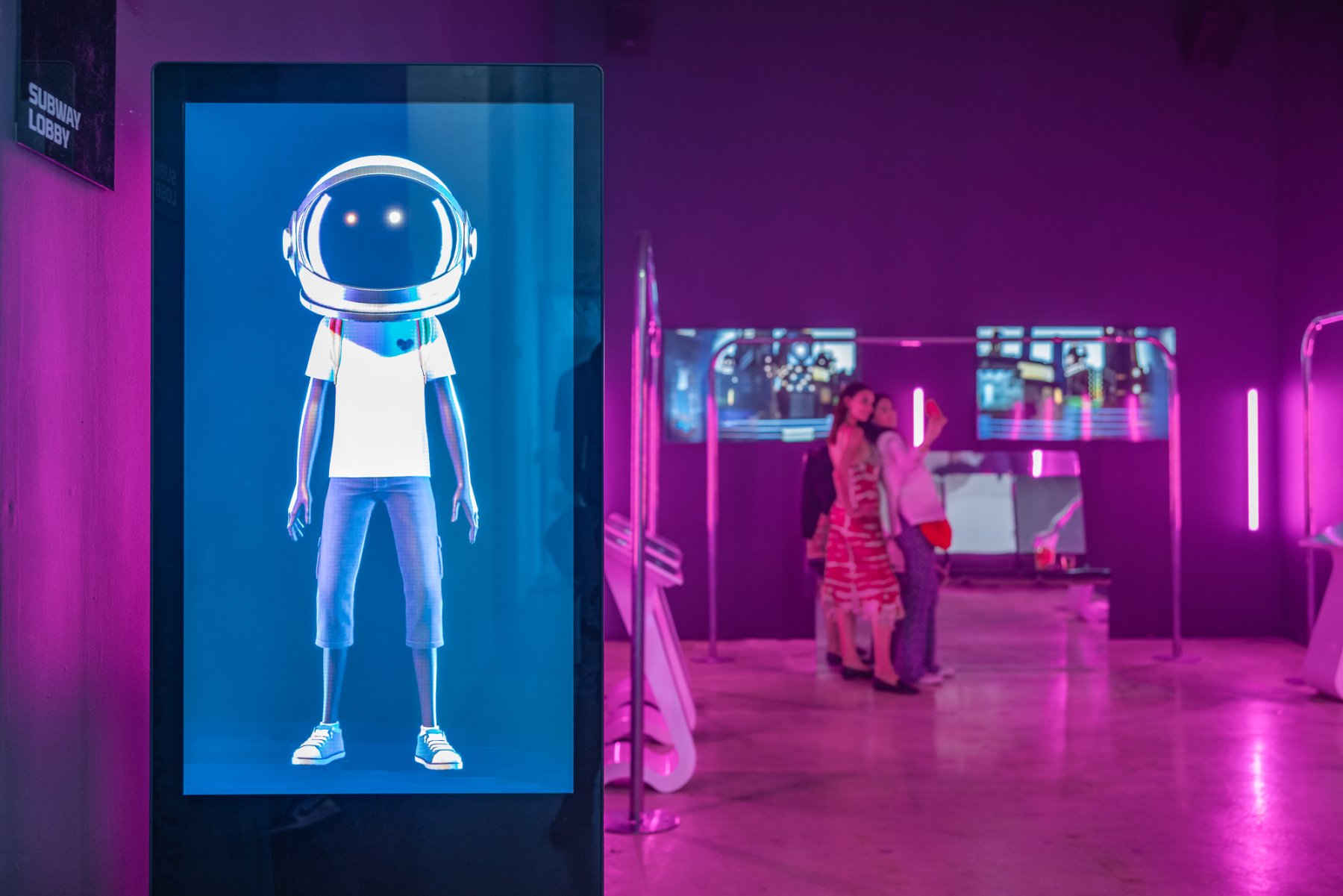 An Aku avatar on a vertical screen by the Subway Lobby, pink-lit room