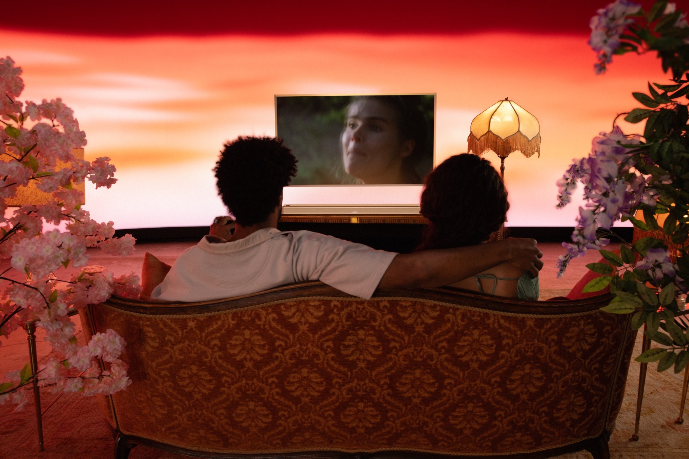 A romance-genre set in warm sunset light, a couple on a couch surrounded by blossom