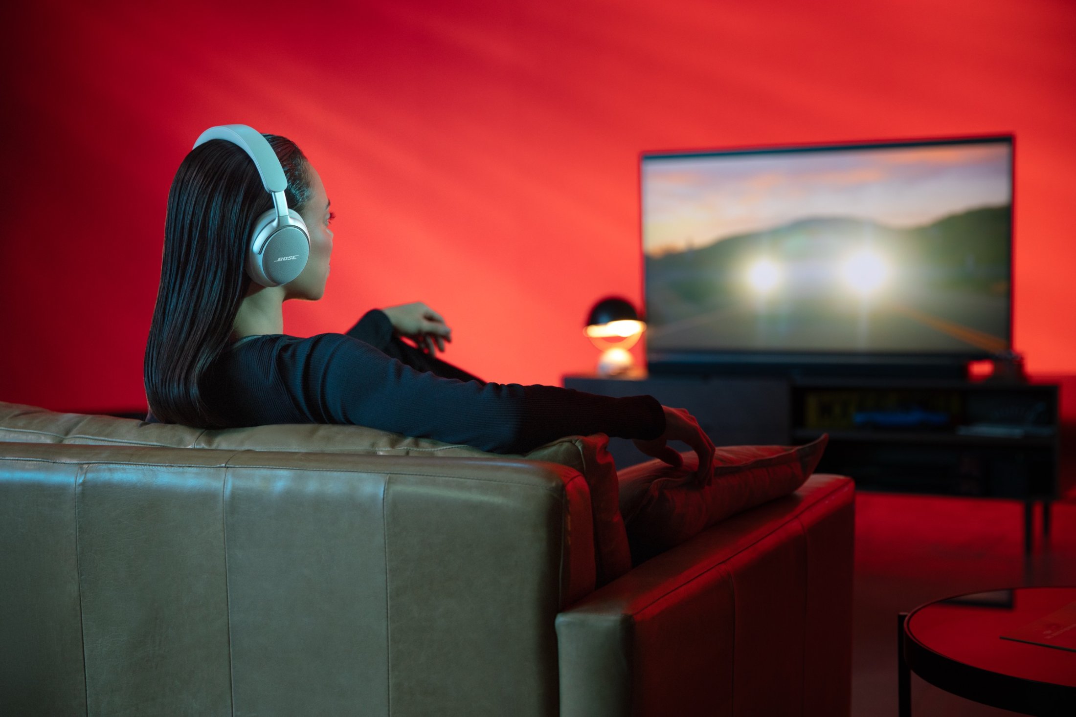 A viewer in Bose headphones watches an action scene in a red-lit room