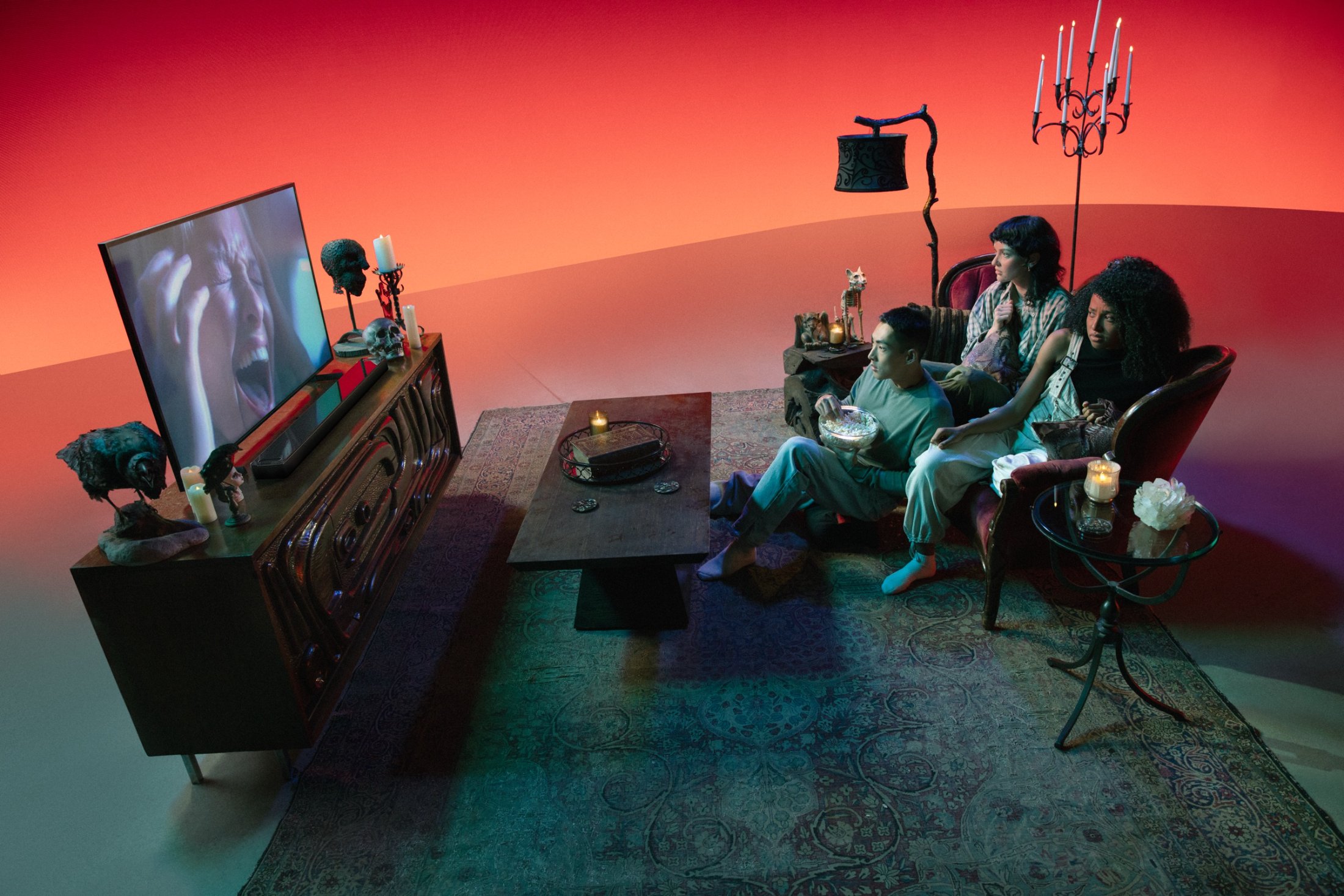 A horror-genre living room set bathed in red, family watching a scream on screen