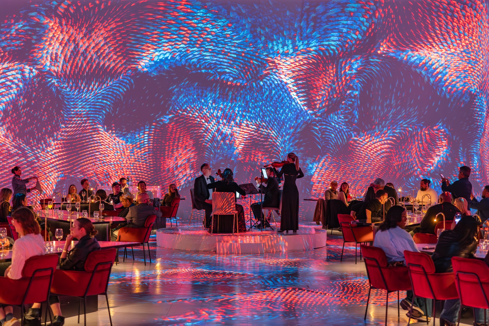 A string trio plays at the center of a room mapped in red and blue waveforms, diners all around