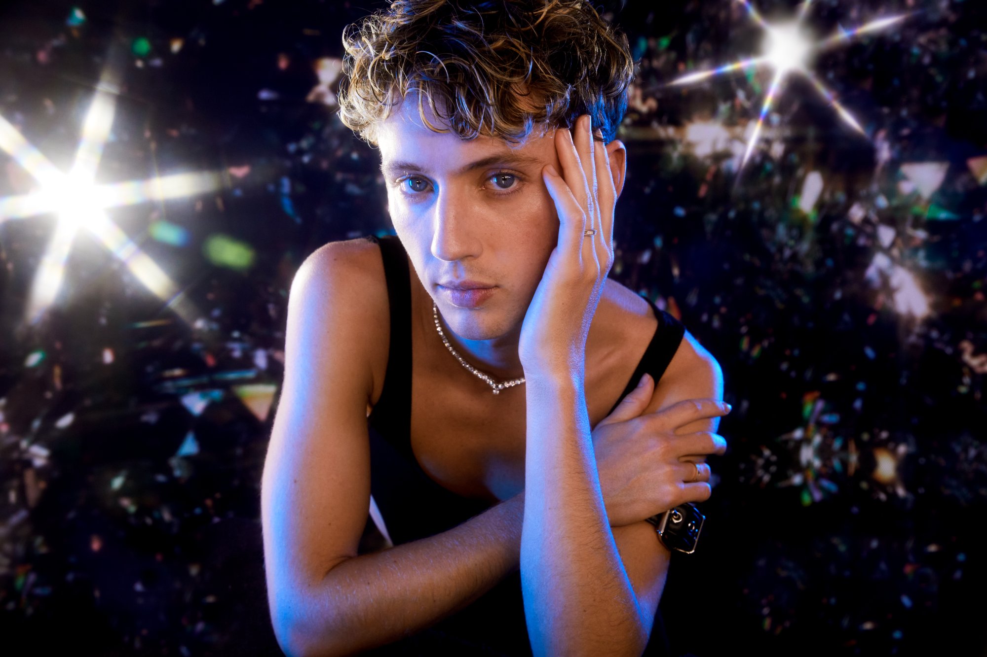 Troye Sivan in a black tank and tennis necklace amid glittering bokeh