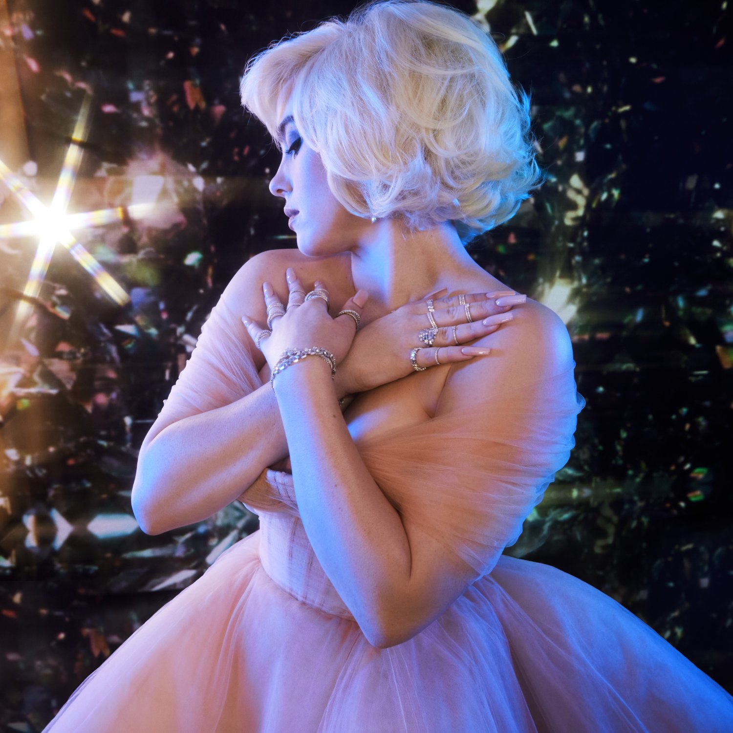 Billie Eilish in a peach gown, arms crossed, rings and bracelets catching light