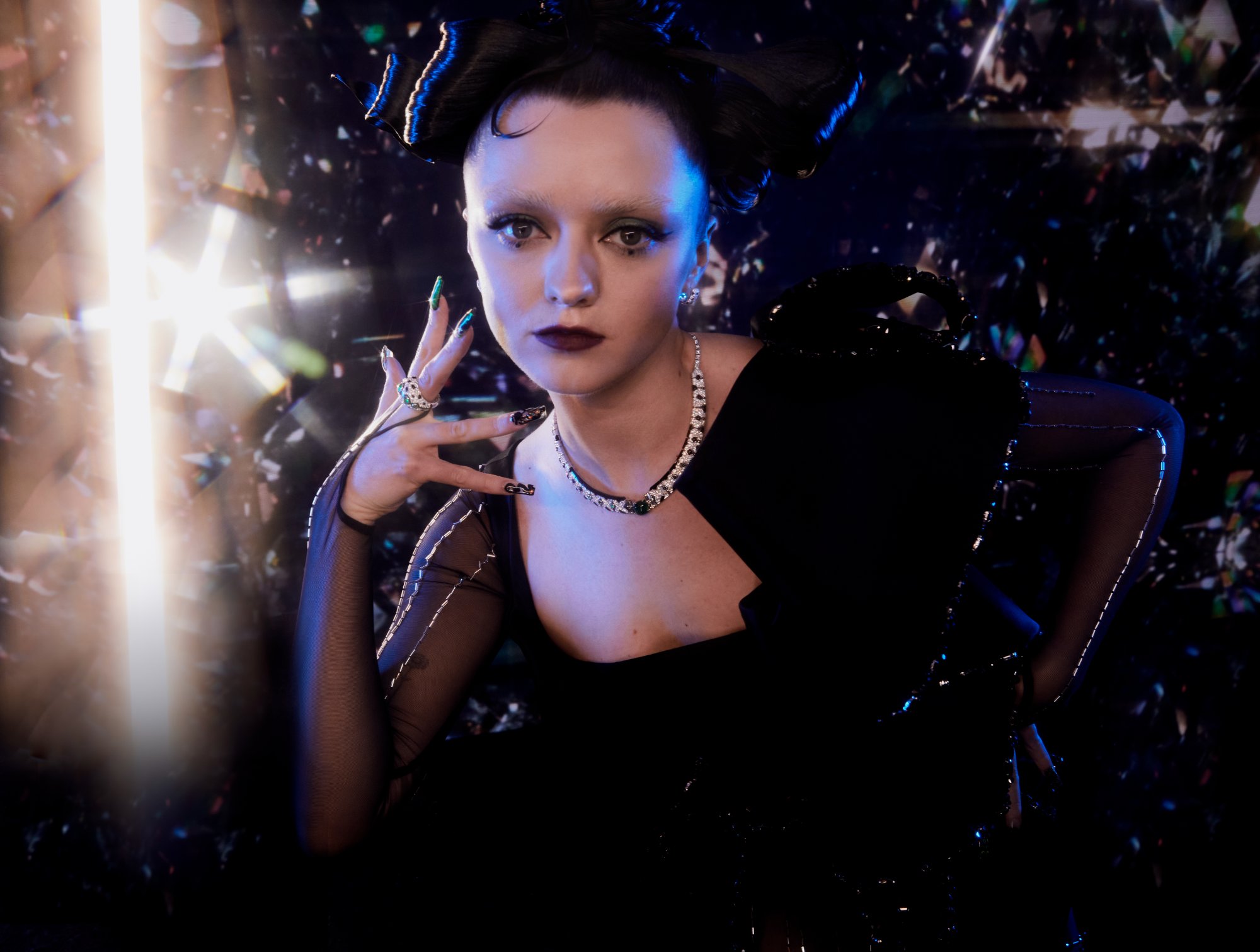 Maisie Williams in black with a diamond necklace, lit by a star of light