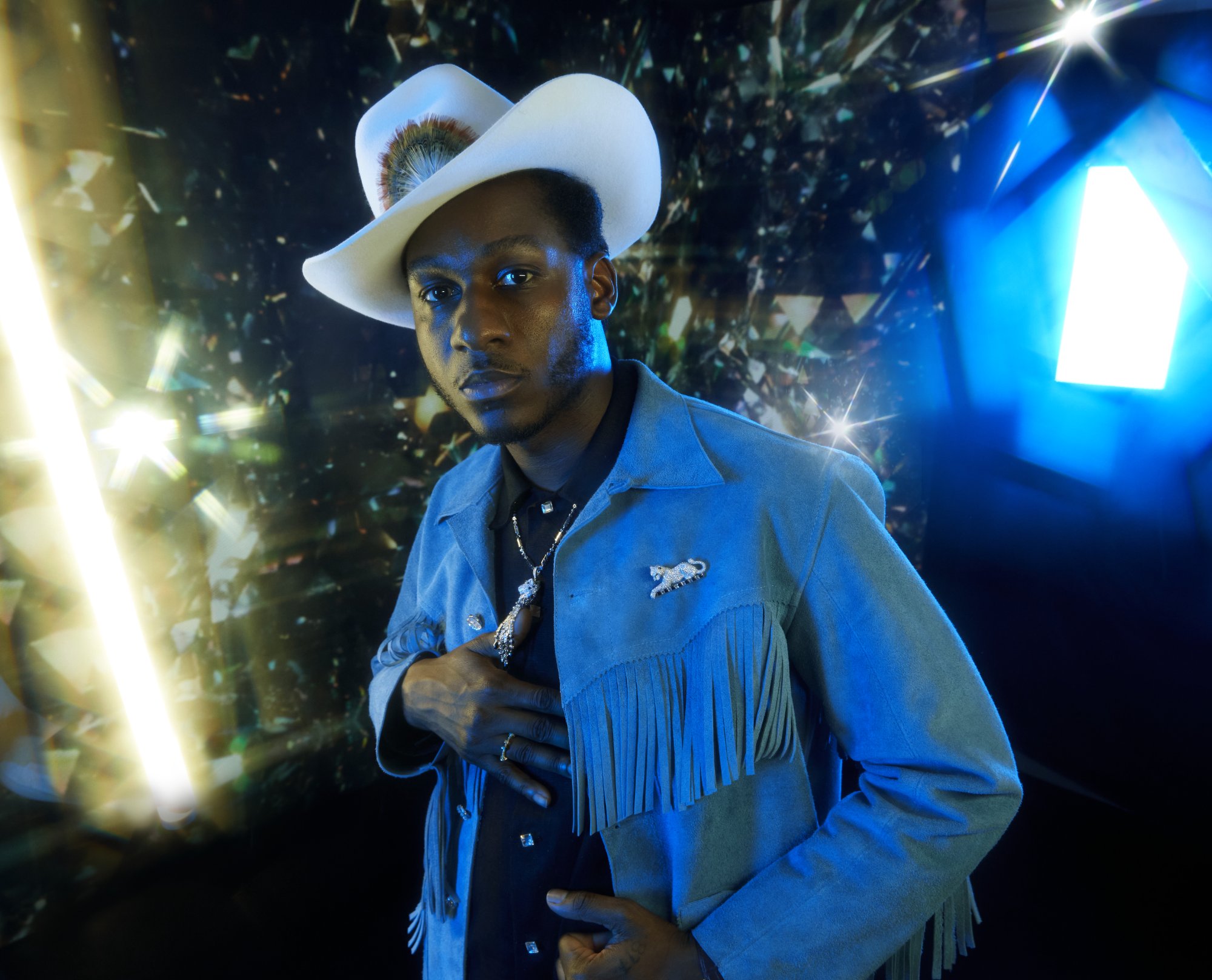 Leon Bridges in a white hat and blue suede, lit by a star of light in the photobooth