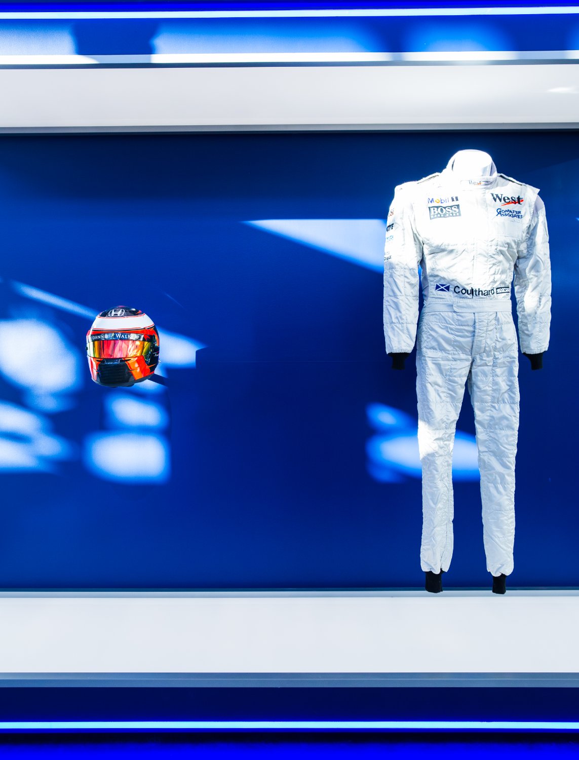 A vintage F1 race suit and helmet shown like a museum piece on blue
