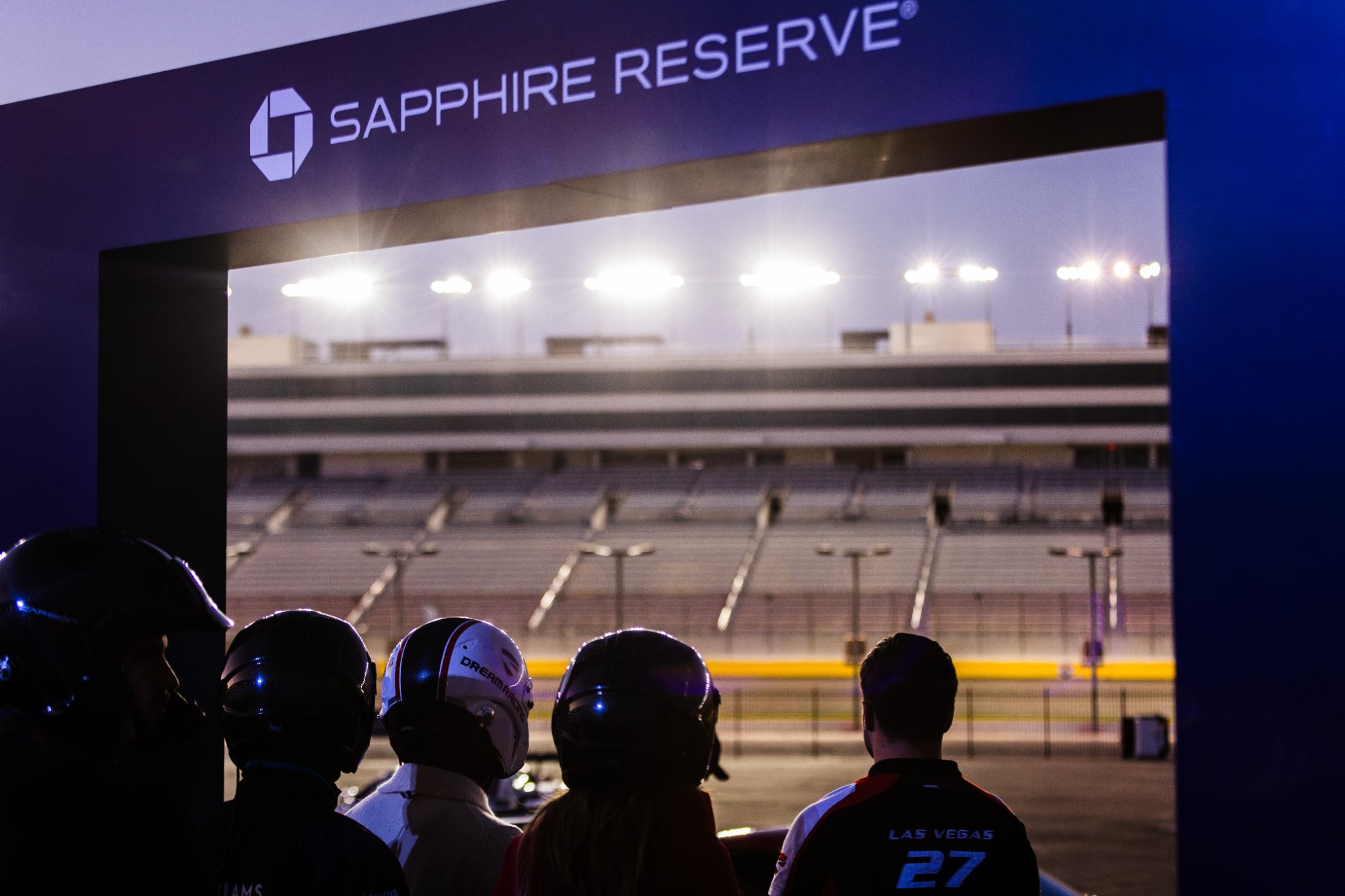 Cardholders in helmets watch the track at night under the Sapphire Reserve arch