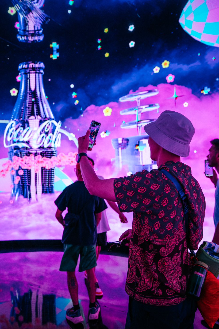 A guest lifts a phone into a galaxy of Coca-Cola towers and floating flowers