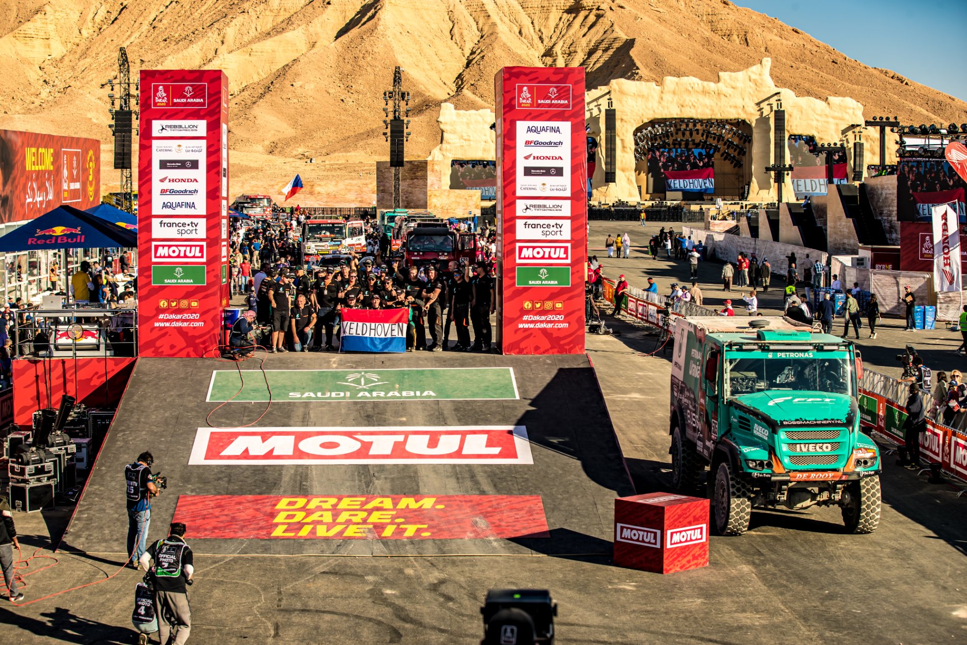 The Dakar finish podium built in open desert, the cliff face of Tuwaiq Mountain rising behind