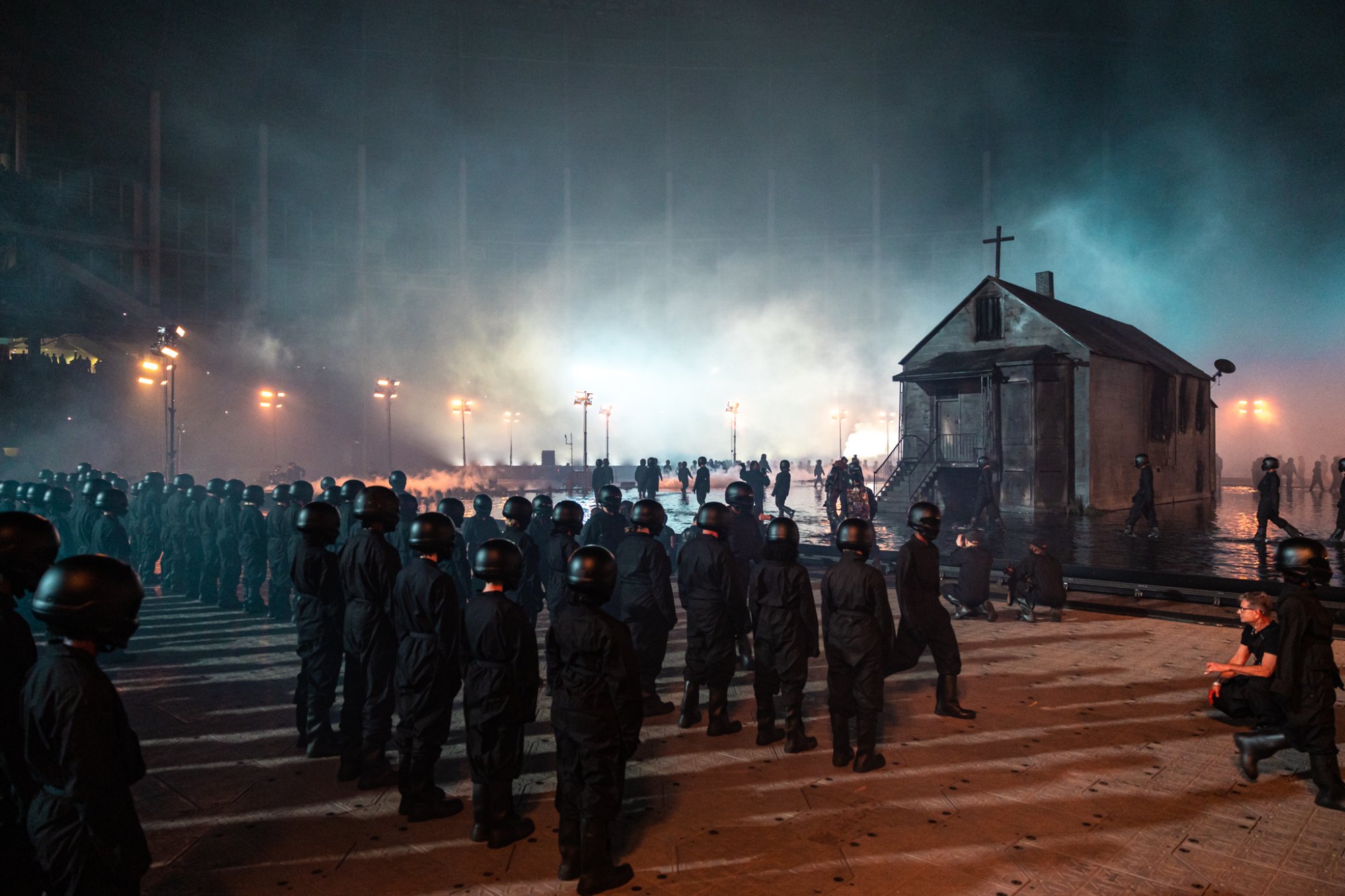 Ranks of helmeted performers face the house across the flooded field