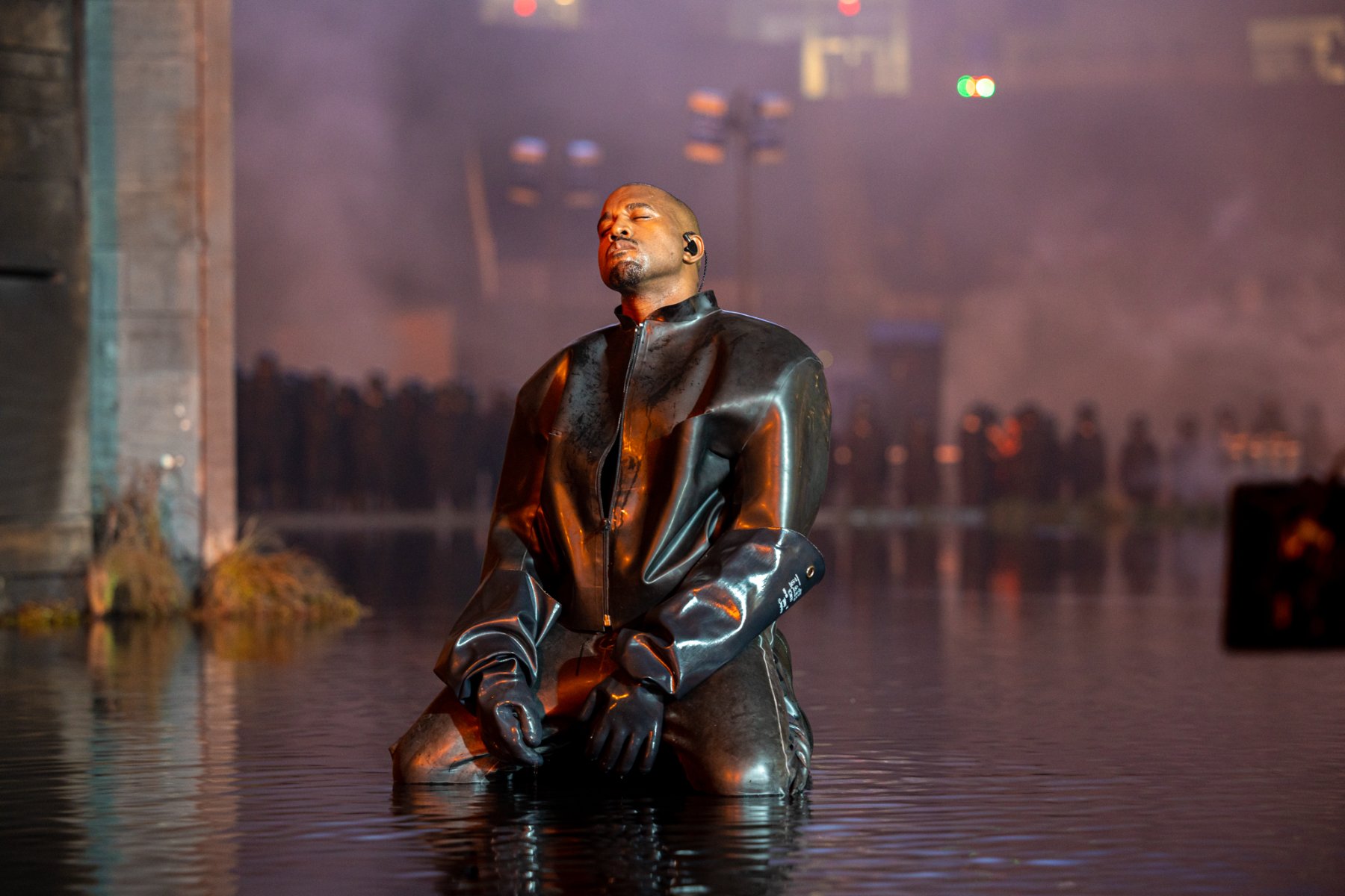Kanye West kneels in the water in black, head bowed