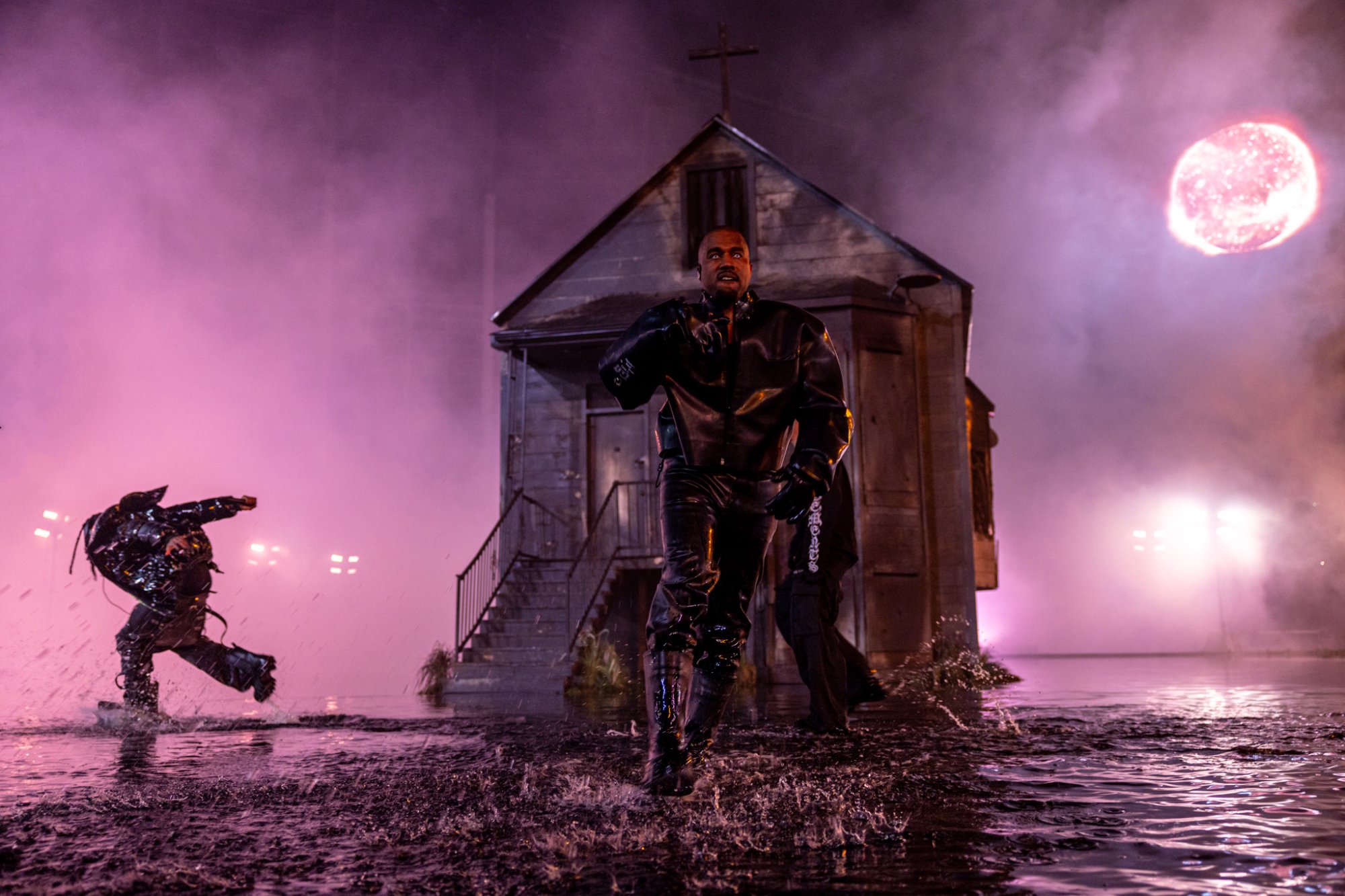 Kanye West runs from the house through pink smoke under a blood-red moon