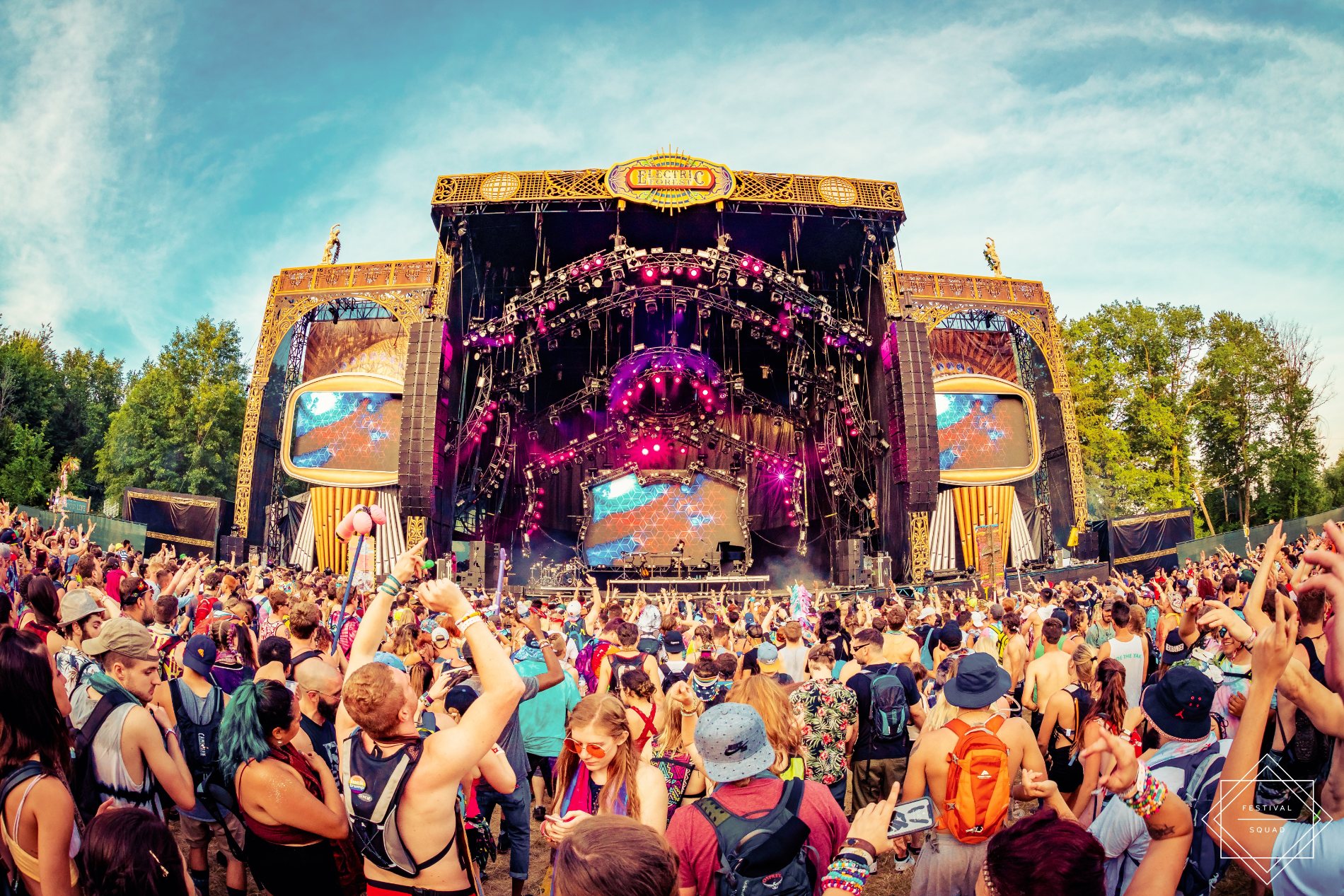 The ornate gold Ranch Arena stage in daylight, the forest behind a sea of fans