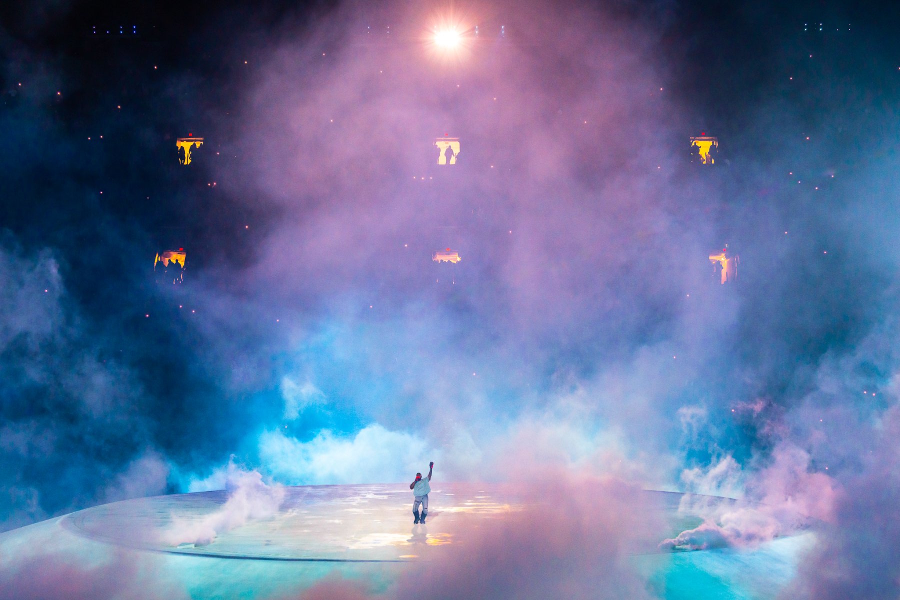 A figure with arms raised on the Mound, blue and pink smoke, lit platforms above