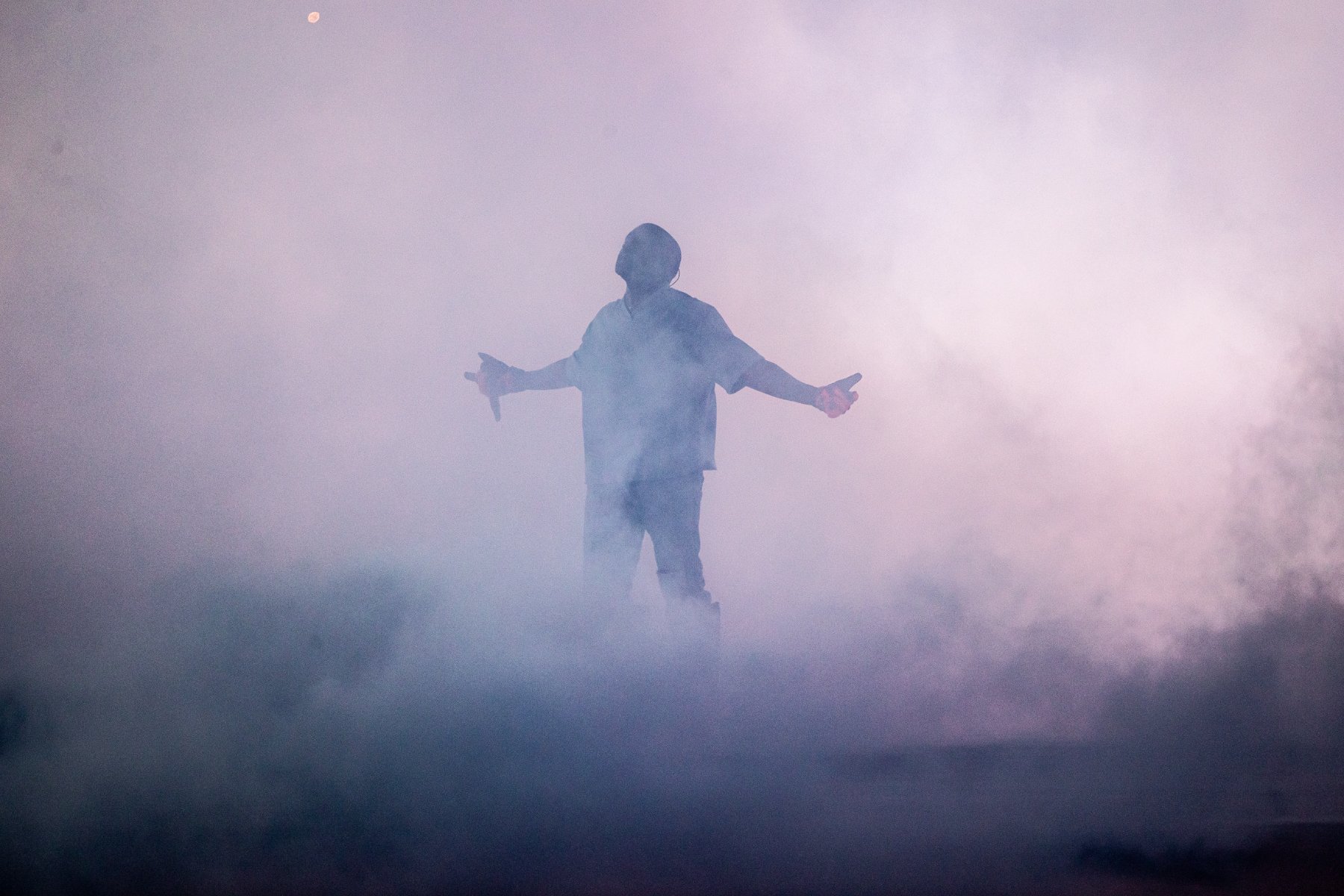 A lone figure, arms outstretched, enveloped in pale blue smoke