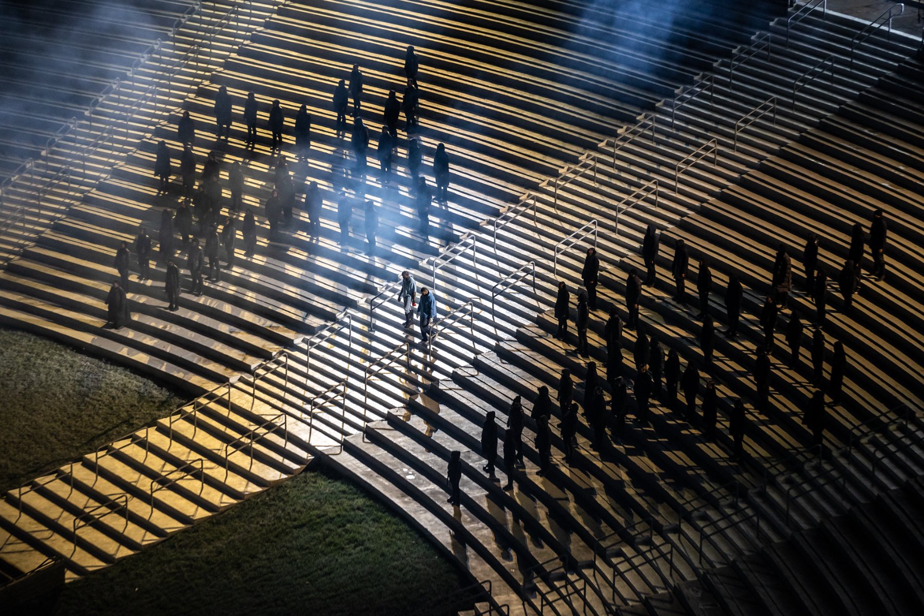 Figures arranged across the lit peristyle steps, beams cutting through