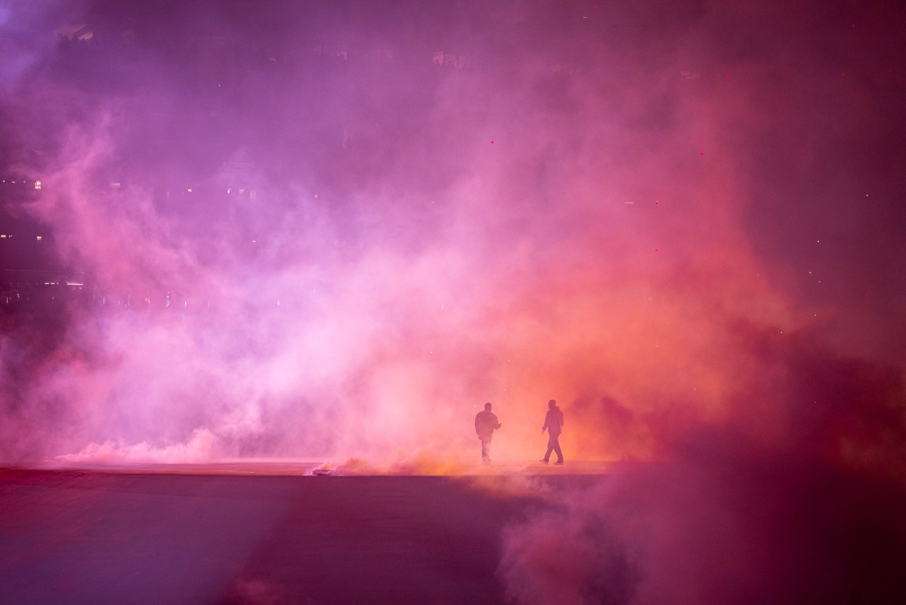 Two figures cross the field through a wall of pink and orange smoke