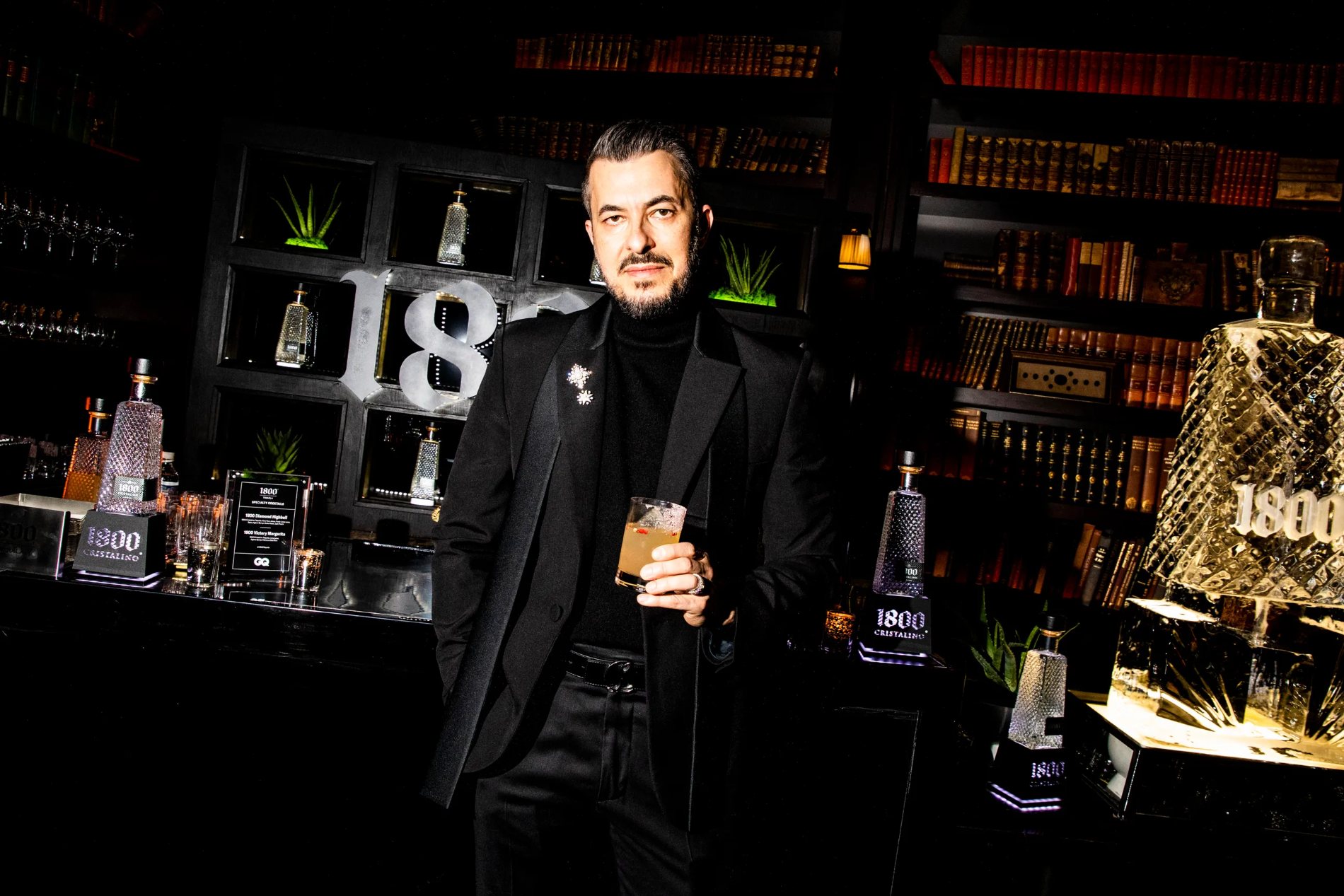 A guest in black holds a cocktail beside the 1800 ice sculpture in the Nomad Library