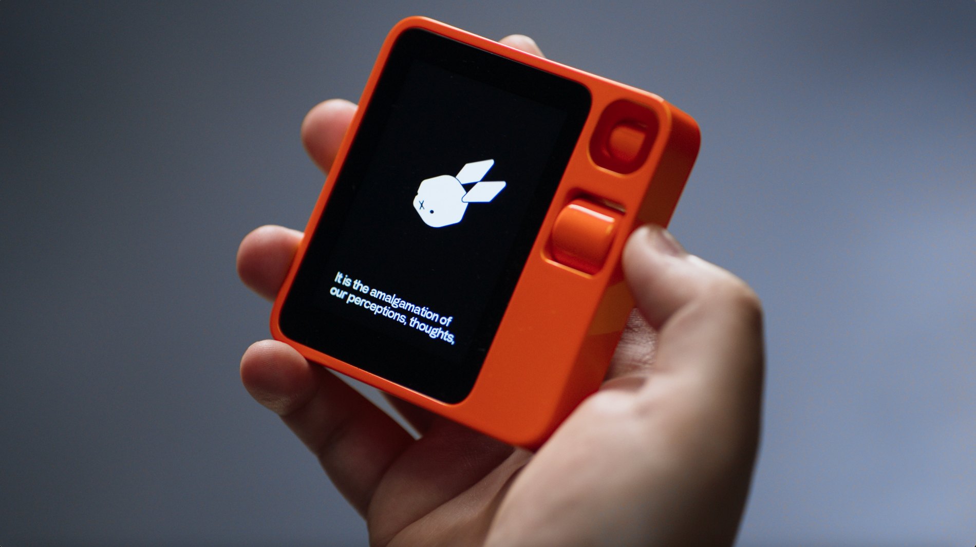 The orange Rabbit r1 held in hand, its boot animation on the screen