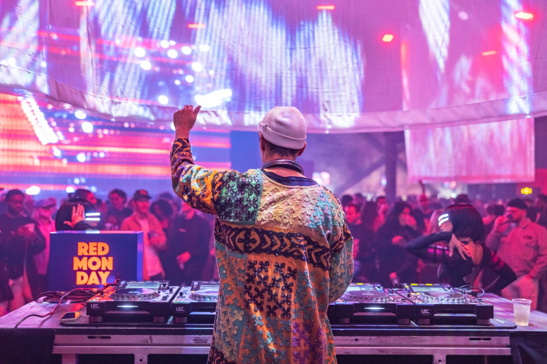 A DJ in a patterned coat works the Red Monday booth over the floor
