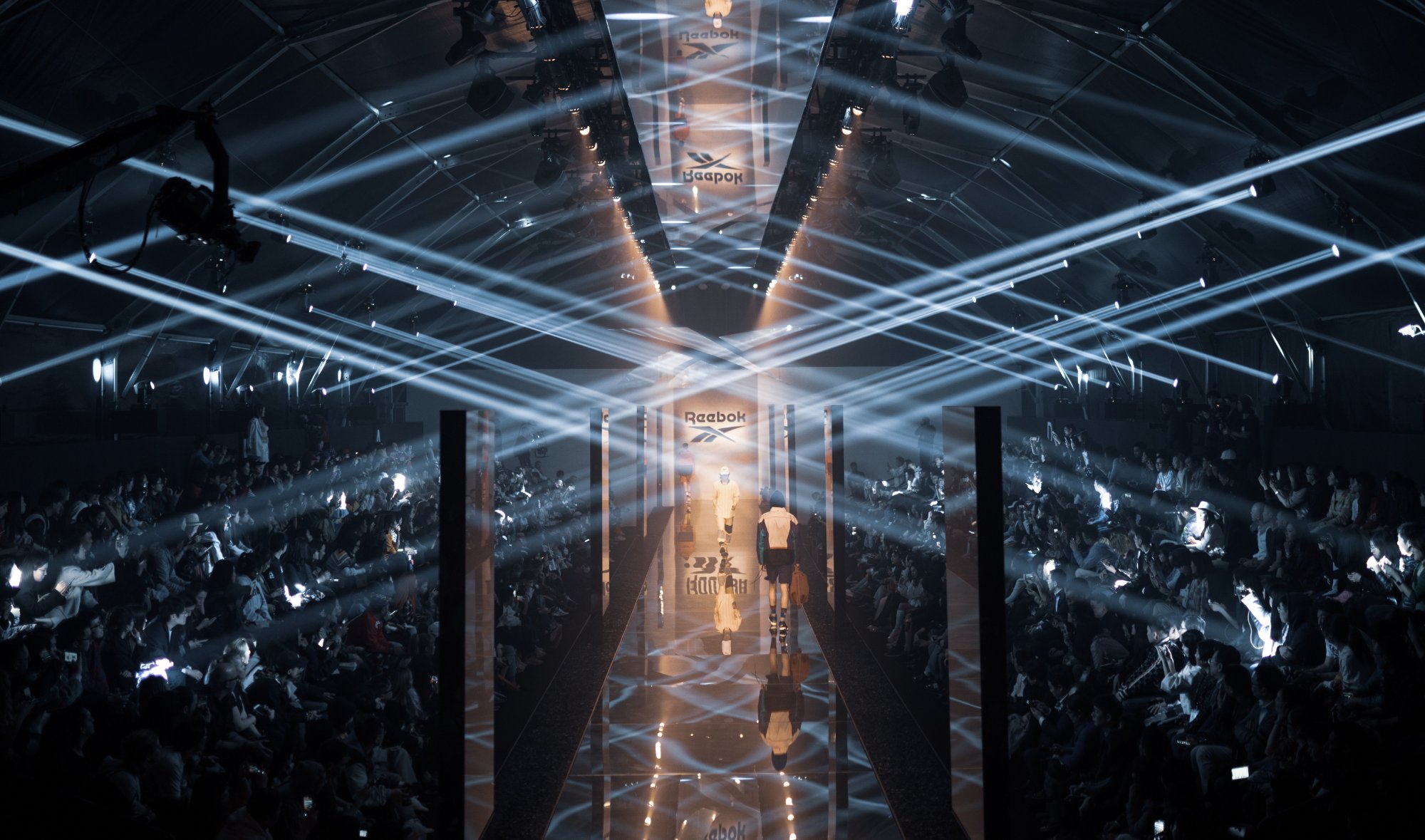 Overhead view of the mirrored runway, beams crossing in an X over the crowd