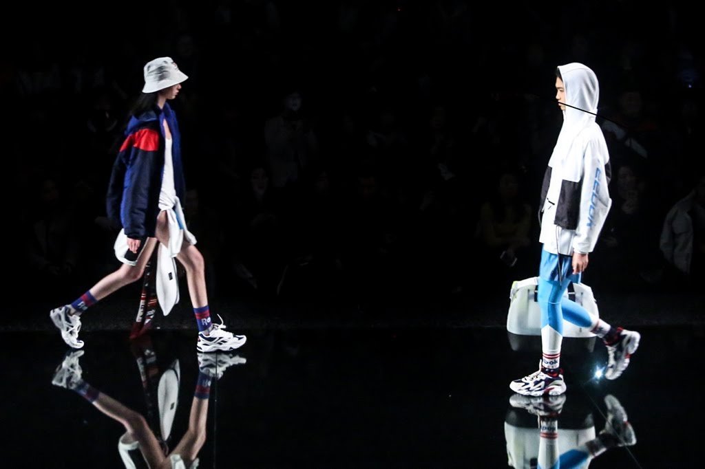 Two models reflected on the black mirrored runway floor