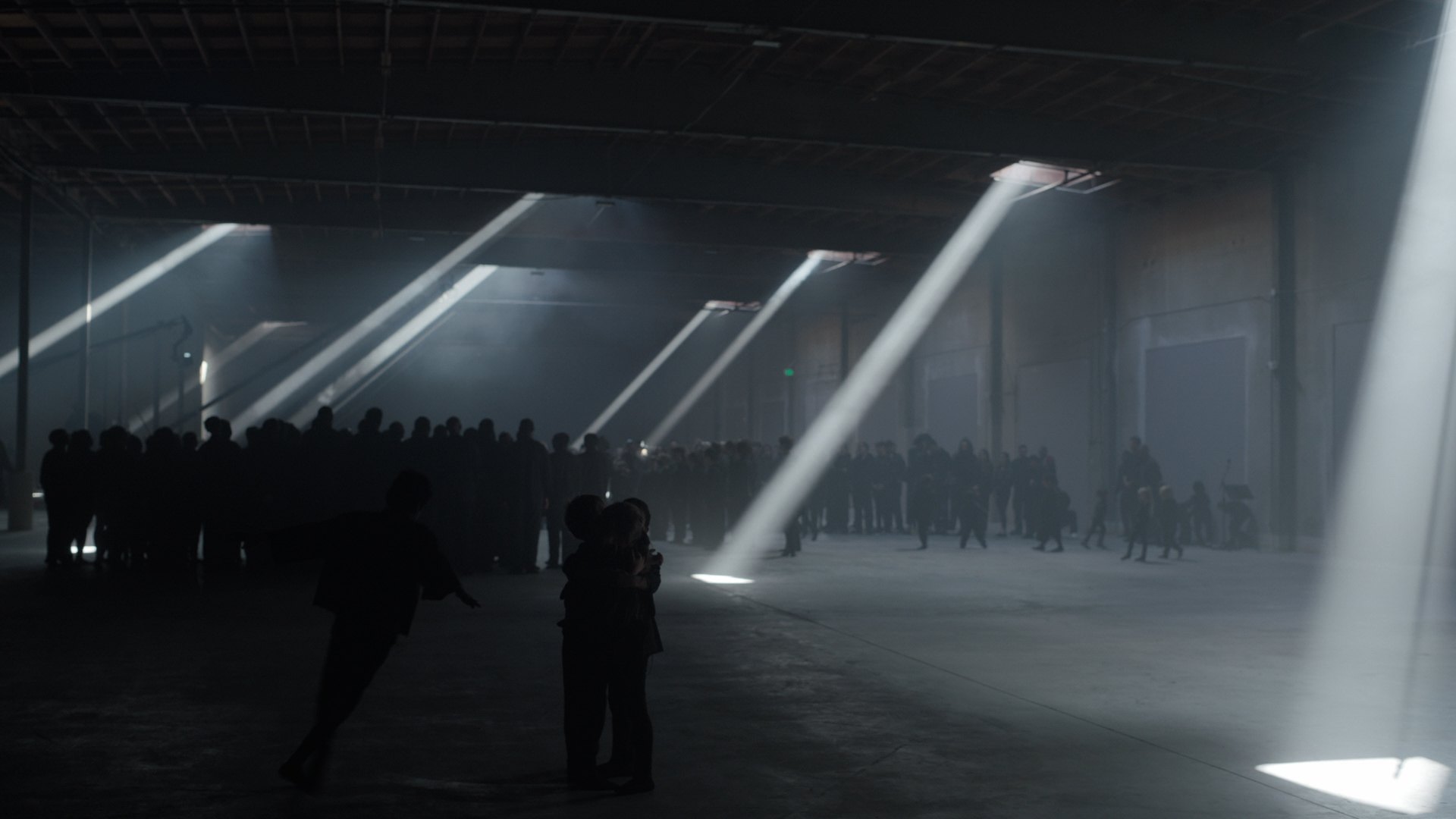 Shafts of light cut through a darkened warehouse over a standing congregation