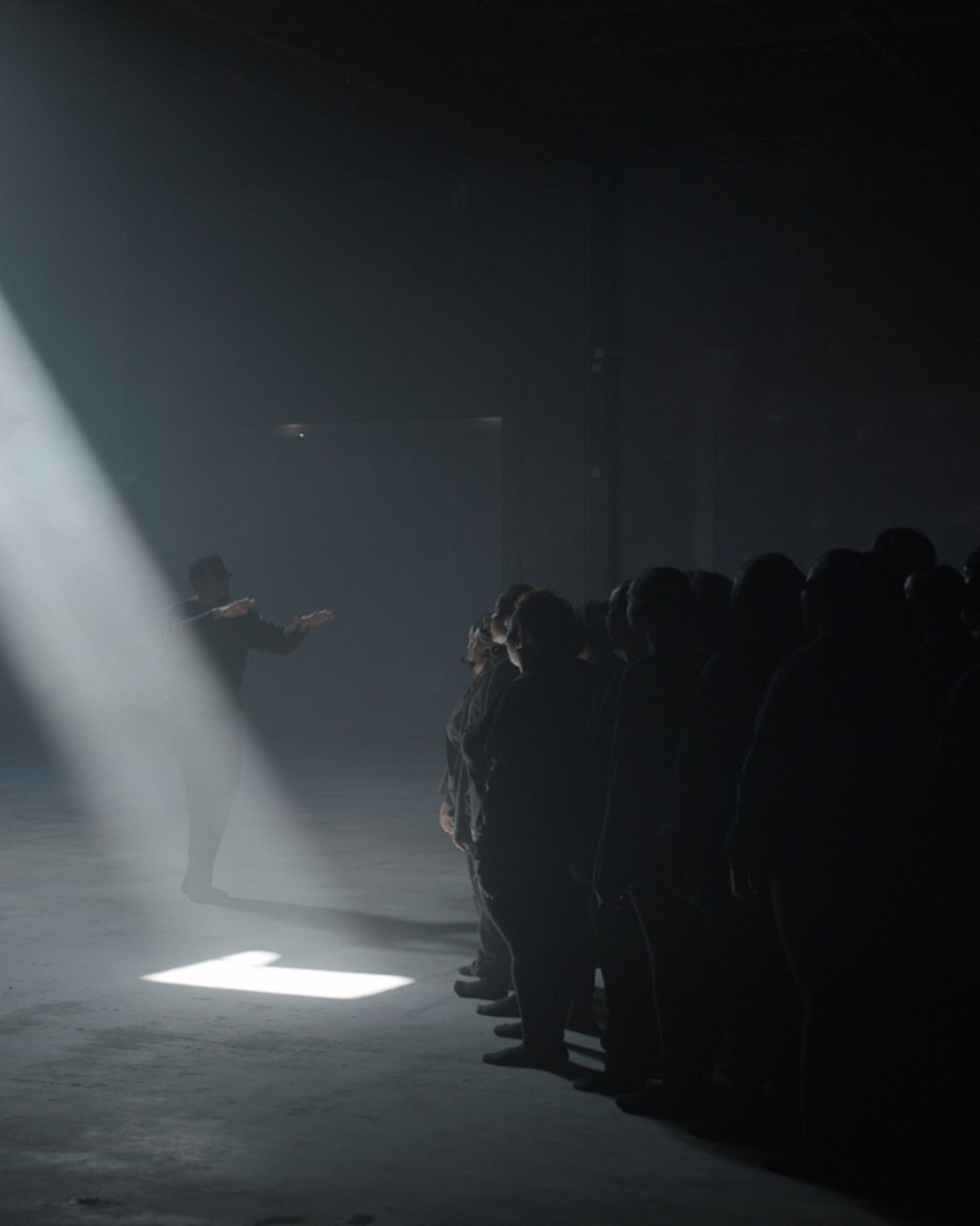 A lone figure steps into the beam as the choir stands in shadow