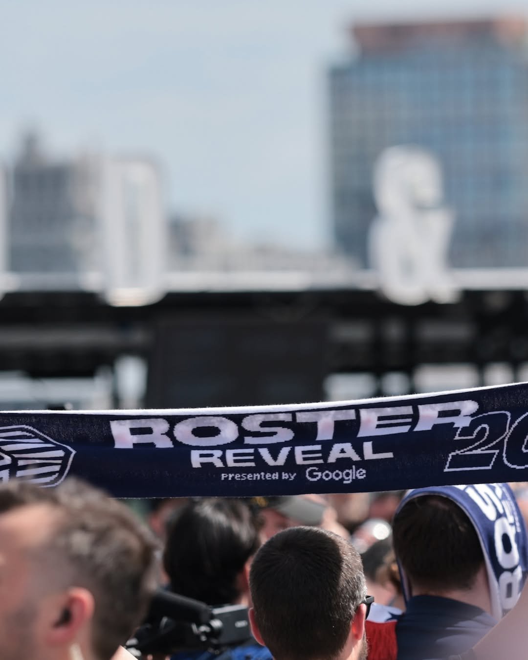 A Roster Reveal 2026 scarf held up against the city skyline